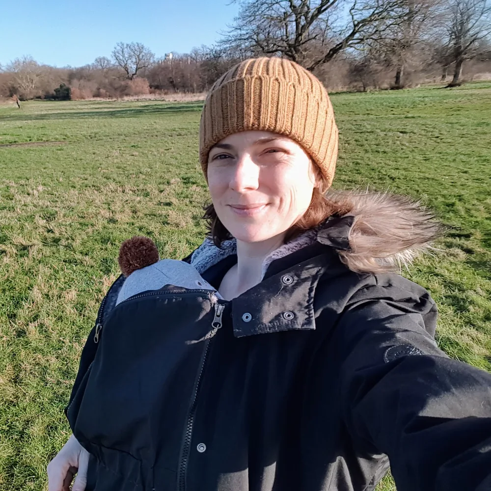 Elodie walking in an East London park with her baby in a carrier